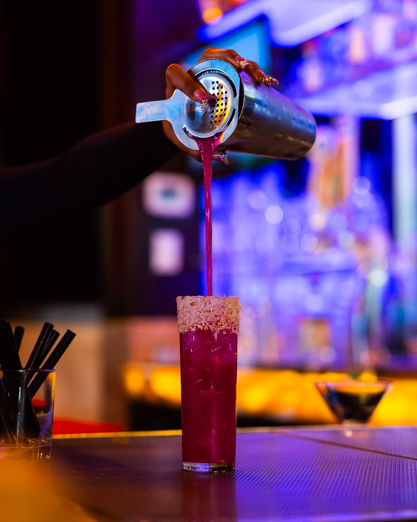 Bartender straining a magenta cocktail into a coconut-rimmed glass at the Vintage 423 bar
