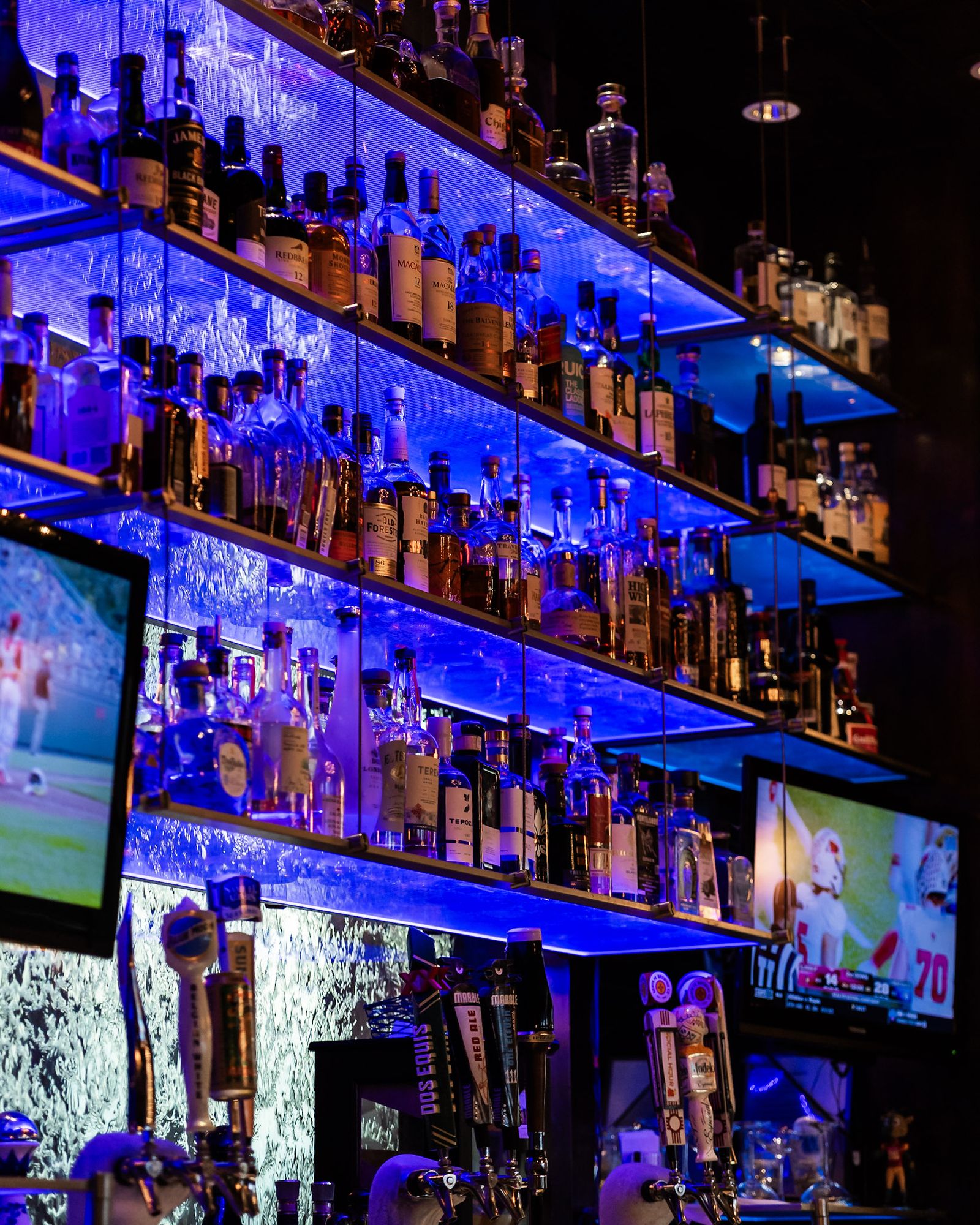 Back bar shelving lined with spirits under blue LED lighting